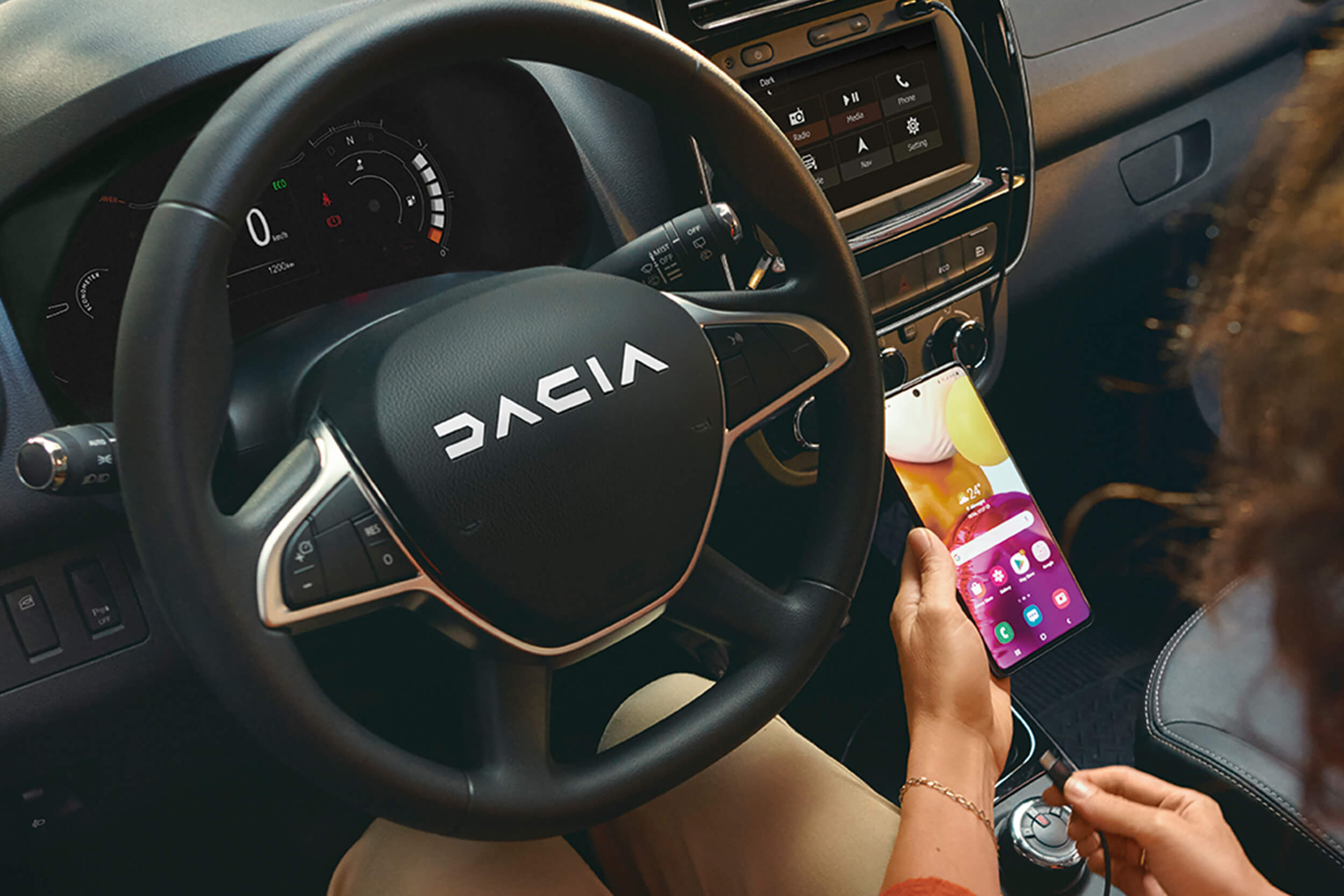 Moteris sėdi prie elektrinio Dacia Spring vairo ir laiko telefoną, susietą per Android Auto